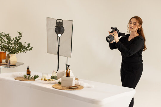 Woman photographer in black holding DSLR with mic, framing with amber bottles in studio, copy space
