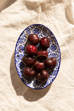 overhead shot of deep red cherries on a Portugese handmade blue and white dish on a light linen tablecloth