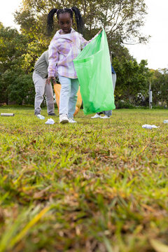 Family cleaning park, youth female walking toward camera holding translucent green trash bag
