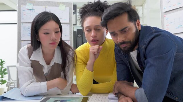 Three colleagues huddled closely together, reviewing a data analytics chart on a tablet screen, deeply focused and collaborative moment in a busy modern office.