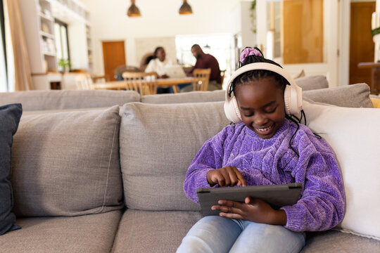 African family gathering in living room, youth on right sofa wearing white headphones using tablet