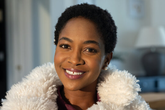 Adult African woman smiling while wearing fluffy white coat and maroon top, showing pearl earring