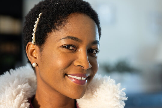 Woman smiling and looking toward camera at home, wearing fluffy white coat collar, pearl hair clip