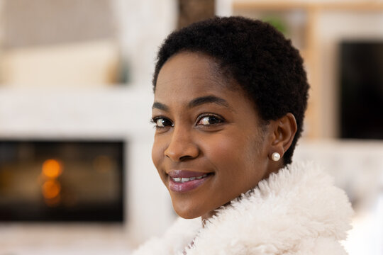 Woman smiling, looking at camera by fireplace, wearing white fluffy coat and pearl stud earring