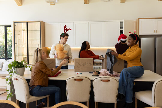 Diverse volunteers packing donation boxes at kitchen island, holding teddy bear and tape