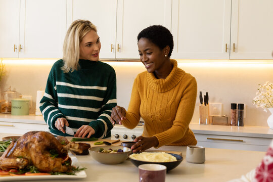 Diverse women preparing meal in kitchen wearing striped sweater and turtleneck with roasted turkey