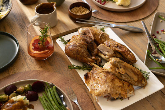 Carved roasted poultry is resting on rectangular white platter on wooden table, surrounded by sides