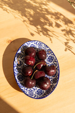 overhead shot of deep red cherries on a Portugese handmade blue and white dish on a light wood table with dappled shadows