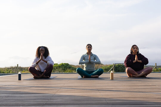 African American women sitting on wooden deck meditating with yoga mats and water bottles