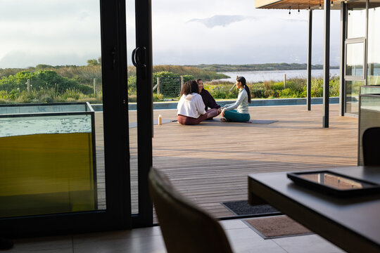 African American women sitting on yoga mats chatting on wooden deck with water bottle in activewear