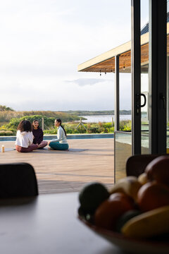 African American women friends sitting on yoga mats in activewear on deck beside pool, copy space