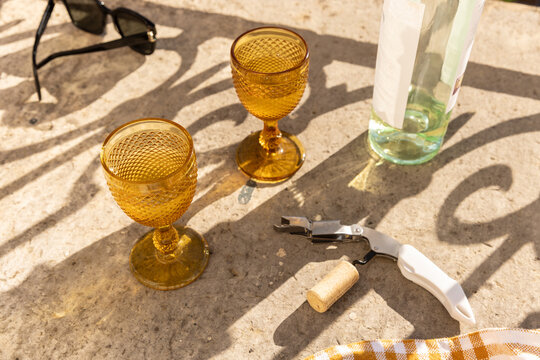 overhead shot of amber gold vintage goblet wine glass with bottle of white wine and wine opener with cork on concrete surface 