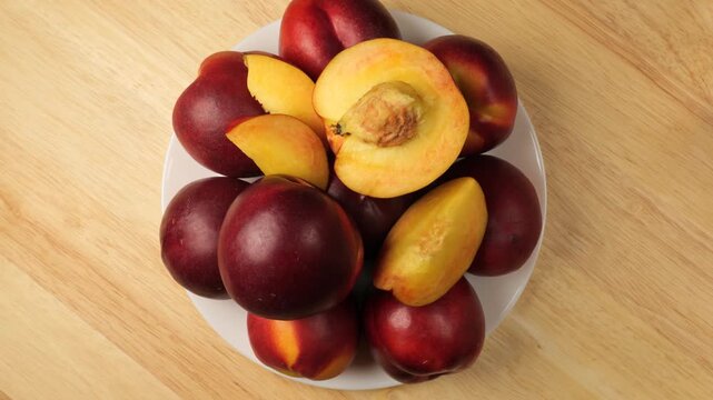 White plate with fresh nectarines rotating on a wooden table