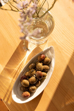 overhead shot of olives in a ceramic handmade plate of olives garnished with salt and dried herbs on a light wood table