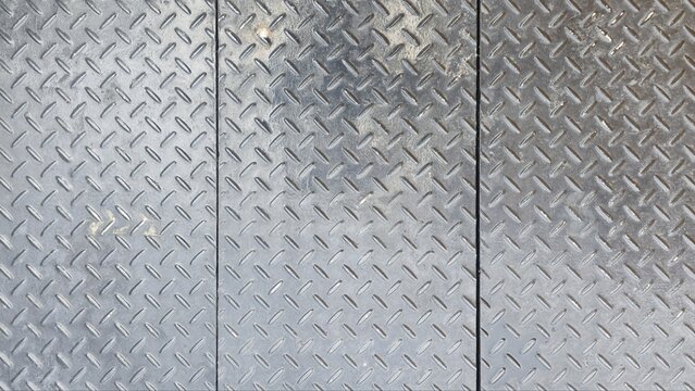 Grey diamond plate steel flooring texture background. Top view of shiny checkered metal sheet with realistic scratches and dark industrial grime marks.