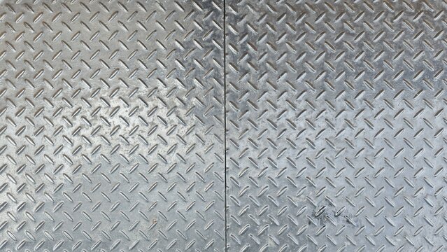 Grey diamond plate steel flooring texture background. Top view of shiny checkered metal sheet with realistic scratches and dark industrial grime marks.