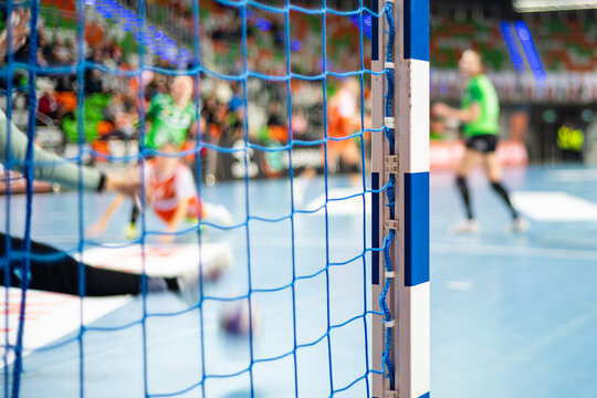 Detail of handball goal post with net and players in the background.