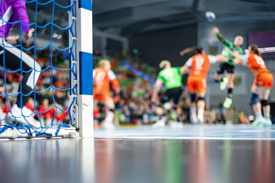 Detail of handball goal post with net and players in the background.