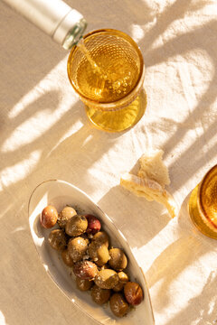 overhead shot of mustard gold wine glasses on linen tablecloth with ceramic handmade plate of olives garnished with salt and dried herbs with dappled shadows in afternoon light