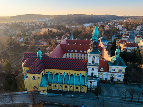 Drone aerial view of the Sanctuary of Saint Hedwig in Trzebnica, Poland, featuring the historic baroque basilica and monastic complex at sunset.