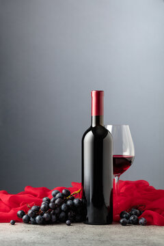 Bottle of red wine with grapes on a grey background.