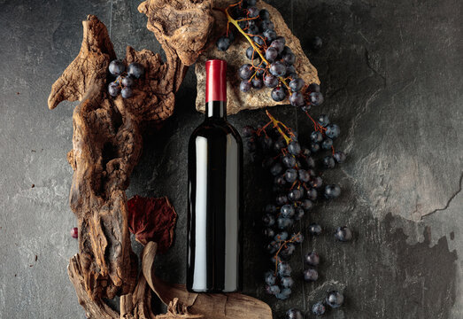 Bottle of red wine with stones, dried snags, and blue grapes.