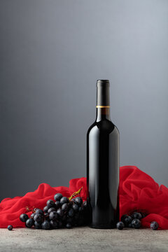 Bottle of red wine with grapes on a grey background.