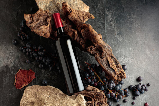Bottle of red wine with stones, dried snags, and blue grapes.