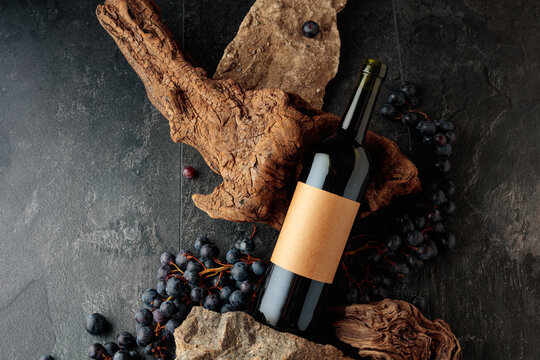 Bottle of red wine with stones, dried snags, and blue grapes.
