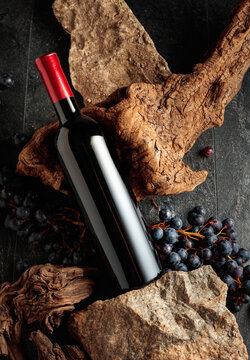 Bottle of red wine with stones, dried snags, and blue grapes.