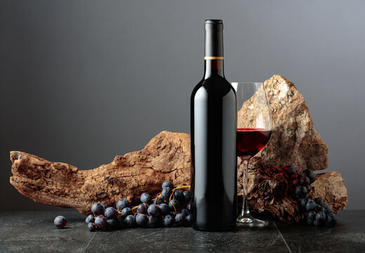 Bottle and glass of red wine on a grey background.