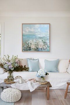 Living room showcasing a cozy interior design, featuring a white slipcover sofa, blue accent pillows, coastal painting, and fresh hydrangeas