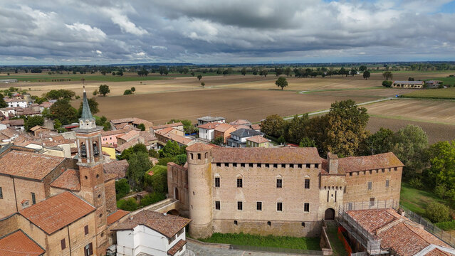 Calendasco Piacenza Emilia Romagna village featuring medieval castle, bell tower, and historic buildings standing over vast agricultural fields and rural landscape under a cloudy sky