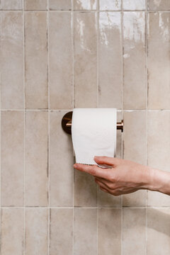Woman taking sheet of soft toilet paper from roll