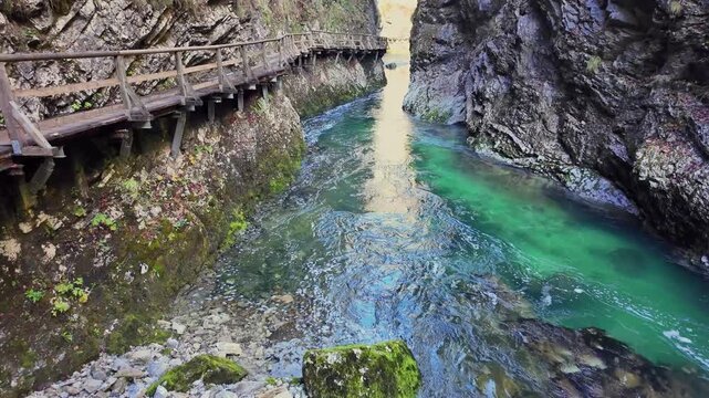 Crystal clear turquoise water of the Radovna River flowing through a narrow canyon alongside a wooden boardwalk in Vintgar Gorge, Slovenia