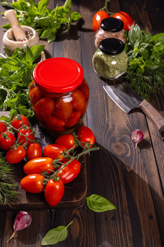 Pickled tomatoes in jar with fresh ingredients on rustic table
