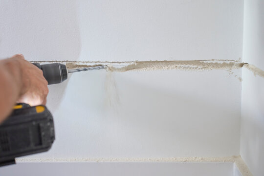 Person drills along channel in interior wall while dust falls from surface