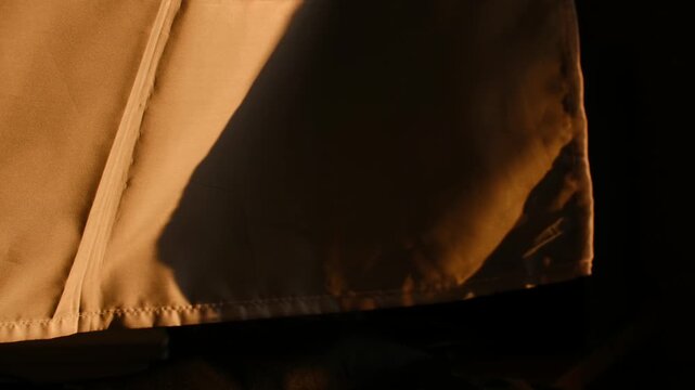 Morning sunbeam moving slowly across fine texture of beige cotton curtain creating an evolving play of light, shadow with warm gentle abstract quality. Golden hour sunlight moving across fabric detail