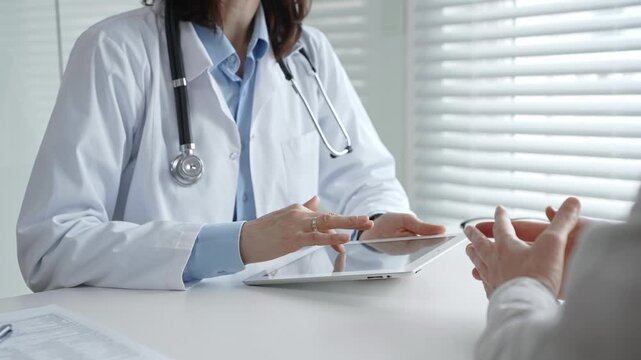 Doctor consulting patient, discussing medical information and diagnosis using a digital tablet during a healthcare visit at a modern clinic office