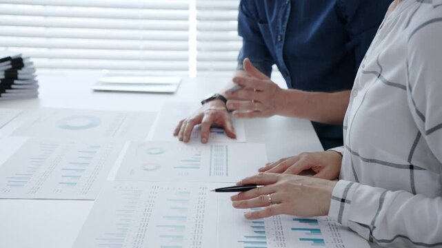 Business professionals analyzing financial data and working together, reviewing charts, graphs, and documents on a white desk during an important office meeting to strategize future growth