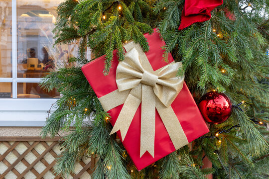 Red Christmas gift with golden bow on decorated tree with lights