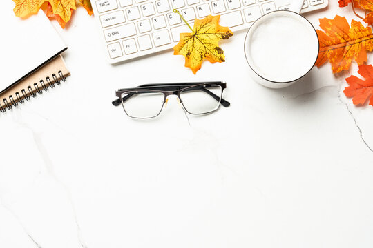 Autumn office desk. Laptop, notebook, hot tea and scarf with yellow leaves.