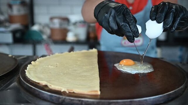 Chef cooking savory crepe with egg on griddle