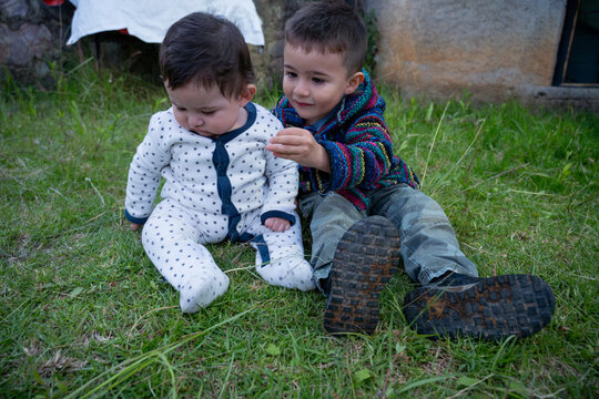 Two cute brothers sitting on the green grass in an outdoor garden.