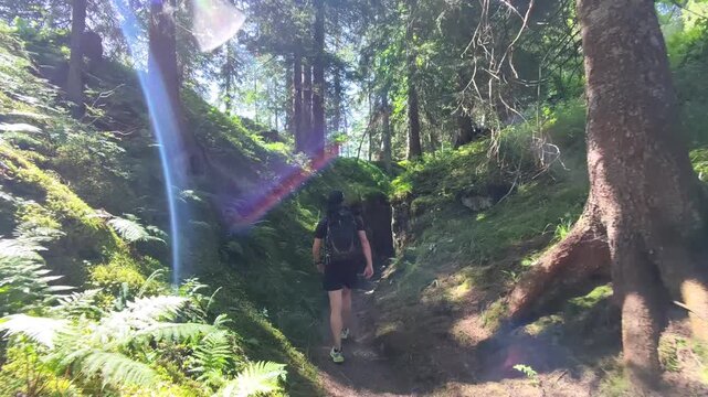 Male hiker walking through a narrow rocky passage near Wirzweli in Central Switzerland, filmed from behind in a dynamic follow-me drone shot surrounded by moss-covered cliffs and forest.
