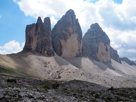 Iconic Tre Cime di Lavaredo, three famous rocky peaks rising above the alpine valley on a sunny summer day. Popular loop hiking route and classic postcard symbol of the Dolomites in Italy.