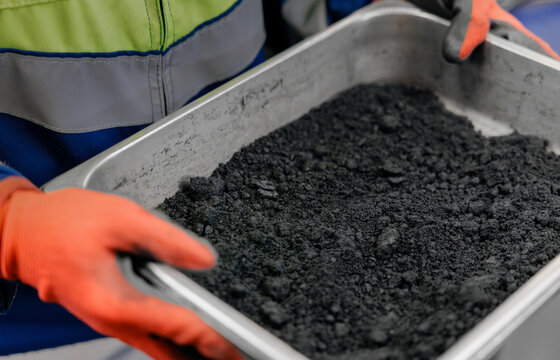 Worker holding metal trays of black powder magnetite iron ore, control quality of mining factory