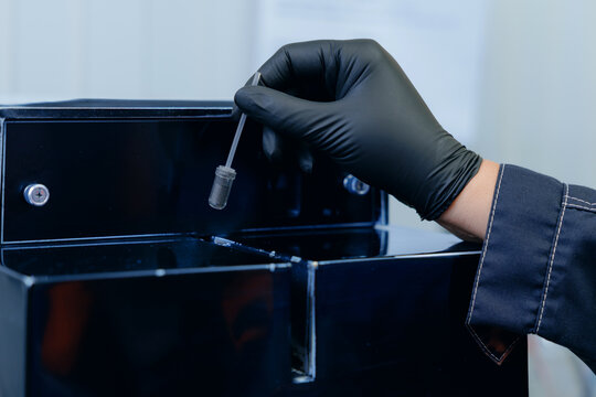 Gloved hands scooping black powder magnetite iron ore into vial on lab bench, control quality of mining factory