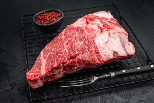 Fresh raw beef shoulder chuck cut with rich marbling on black textured background. BBQ steak meat with seasoning and copy space.