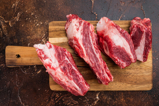 Fresh uncooked beef ribs pieces with bone and fat on cutting board.